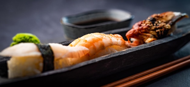 Sushi sashimi con camarones y salsa de soja servido con palillos de madera y wasabi sobre mesa negra ...