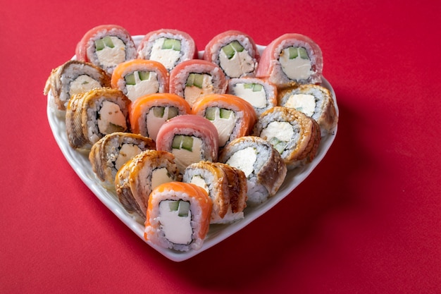 Sushi-Satz von Lachs, Thunfisch und Aal mit Philadelphia-Käse in Platte als Herz auf rotem Hintergrund. Valentinstag Food-Konzept. Nahansicht