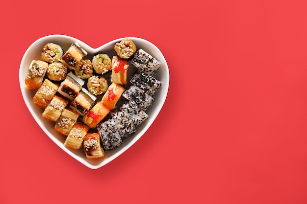 Sushi stellte in Platte als Herz auf rotem Hintergrund ein. Valentinstag Liebeskonzept. Von oben betrachten. Platz für Text. Flach liegen.