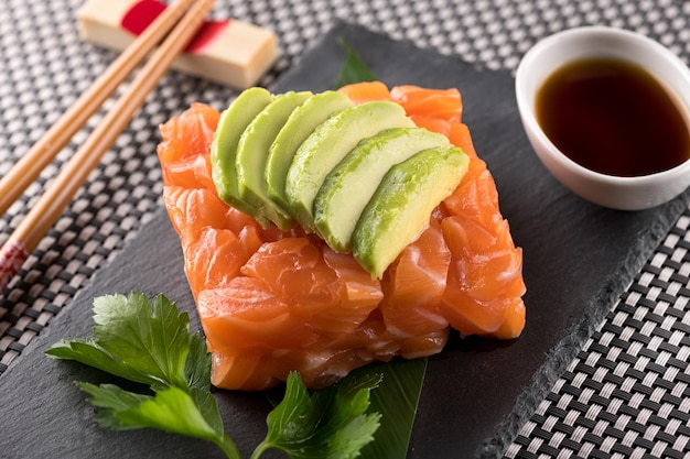 Sushi tártaro de salmão com fatias de abacate, servido com molho de soja em tabuleiro de pedra preta em restaurante japonês