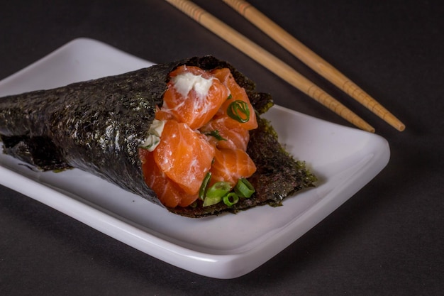 Foto sushi temaki de salmão na chapa branca em fundo preto.