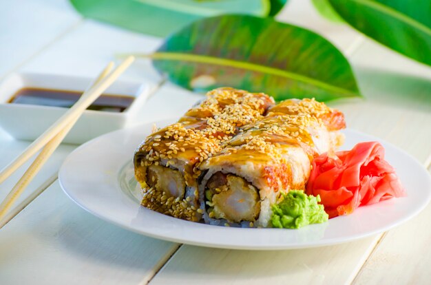 Foto sushi con tempuro de anguila y camarones en un plato y un fondo blanco.