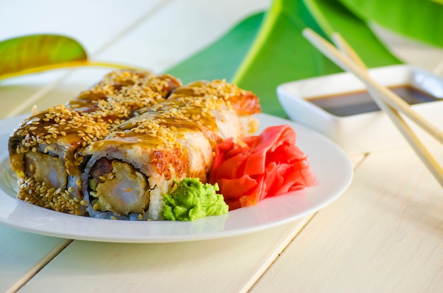 Sushi con tempuro de anguila y camarones en un plato y un fondo blanco.