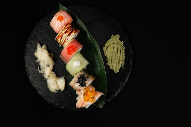 Sushi und gebratene Garnelen mit Knoblauch auf einer Steinplatte mit schwarzem Hintergrund