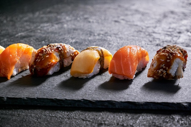 Sushi variado con anguila de salmón y escolar sobre placa de piedra negra sobre fondo oscuro Concepto mínimo