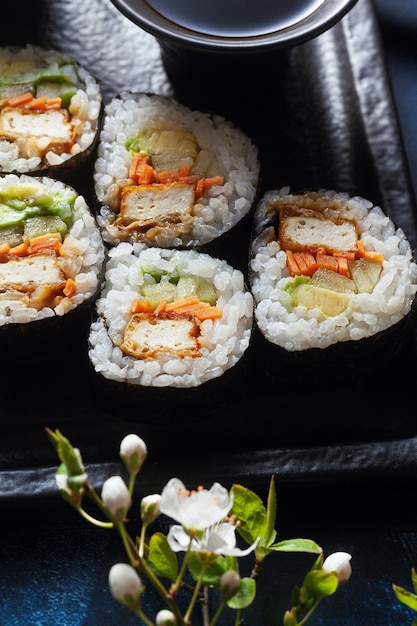 Sushi vegano com tofu em abacate com molho General Tso e legumes frescos em uma mesa com galhos de uma árvore florescente