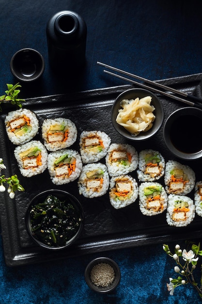 Sushi vegano con tofu en salsa General Tso aguacate y verduras frescas en una mesa con ramas de un árbol floreciente