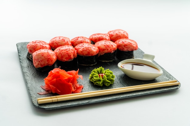 Sushi vermelho em uma superfície preta e branca com wasabi, gengibre, molho de soja e chopstocks