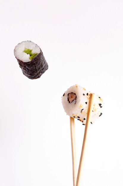 Sushi volador sobre un fondo blanco, sabrosos rollos de sushi, aguacate y palillos