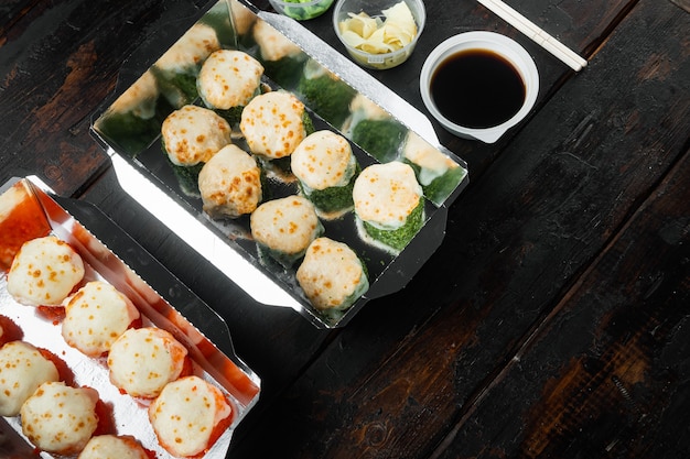 Sushi zum Mitnehmen in Behältern, Philadelphia-Röllchen und gebackene Garnelen auf einem alten dunklen Holztisch