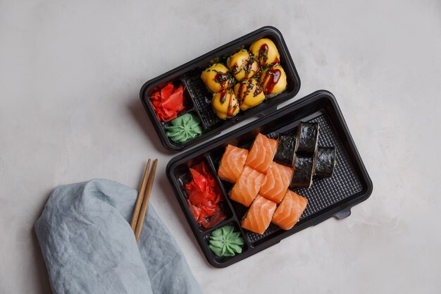Sushi zum Mitnehmen in Plastikbehältern, verschiedene Brötchen, Sojasauce, rosa Ingwer, Wasabi, Sushi-Lieferkonzept. Bestellung von Lebensmitteln