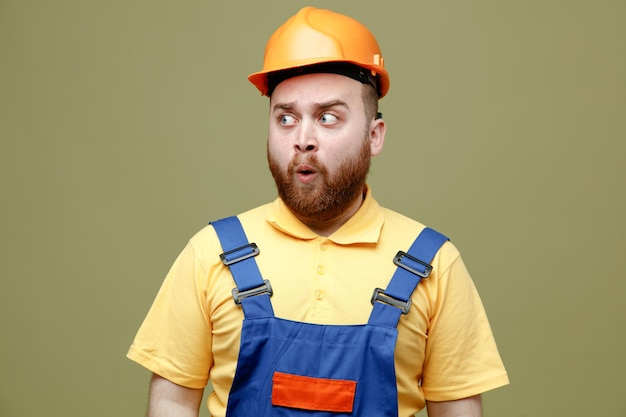 Suspeito olhando para o lado jovem construtor de uniforme isolado em fundo verde