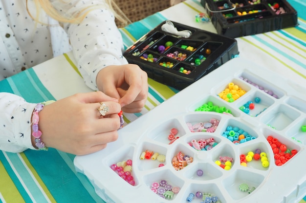 Foto sustratos de plástico con cuentas multicolores y las manos de una niña haciendo un brazalete. hecho a mano, pasatiempos.