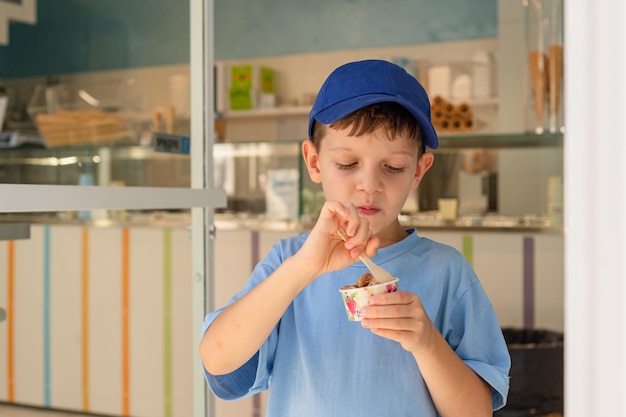 Sute, un niño de 6 años con una camiseta azul, come helado helado con una cuchara de un vaso en una heladería en Roma Turismo tradicional de postres con niños