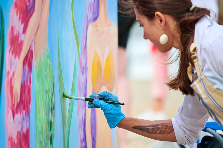 Foto svetlogorsk rusia 08152021 mujer pintora en guantes azules pintando un hermoso cuadro con pincel mezclando pinturas de diferentes colores pintura acrílica en el festival de arte al aire libre
