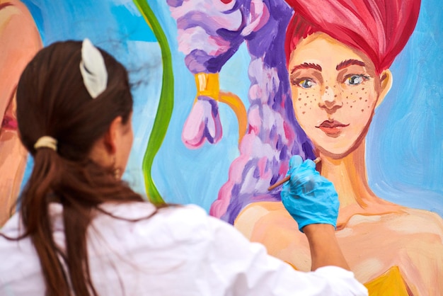 Svetlogorsk Rússia 08152021 Artista feminina pintando com pincel na placa de lona de madeira no festival ao ar livre jovem pintor criando imagem surreal com pincel nas cores azuis roxas e vermelhas