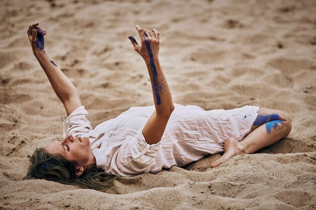 Svetlogorsk Rússia 08152021 Performance de dança de arte feminina na praia de areia Dançarina de mulher deitada de costas na areia e movendo as mãos na performance de arte ao ar livre ao ar livre Dança lenta expressiva