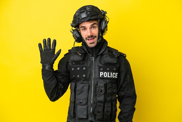 SWAT kaukasischer Mann isoliert auf gelbem Hintergrund, der mit der Hand mit glücklichem Ausdruck salutiert