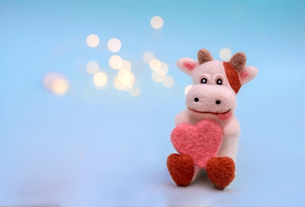 Symbol von 2021, ein Spielzeug fühlte Stier oder Kuh mit Herz auf einem festlichen hellblauen Hintergrund mit Bokeh, mit einem Kopienraum