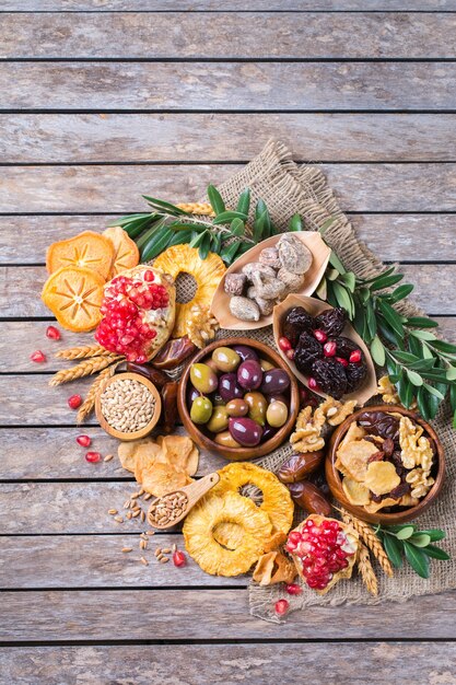 Symbole des jüdischen Feiertags Tu Bishvat, Rosh Hashana neues Jahr der Bäume. Mischung aus getrockneten Früchten, Datteln, Feigen, Trauben, Gerste, Weizen, Oliven, Granatapfel auf einem Holztisch. Kopieren Sie den flachen Hintergrund des Raums