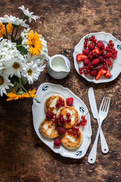 Syrniki mit roter Johannisbeere, Himbeere und Sauerrahm auf dem hölzernen Hintergrund Draufsicht Köstlicher Frühstücksbrunch