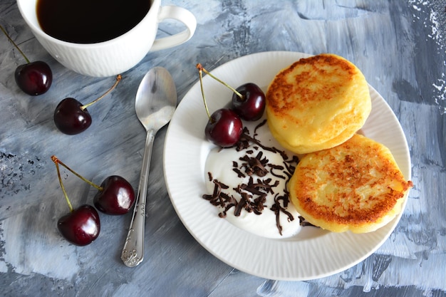 Syrniki ucraniano con cerezas en plato blanco aislado, primer plano