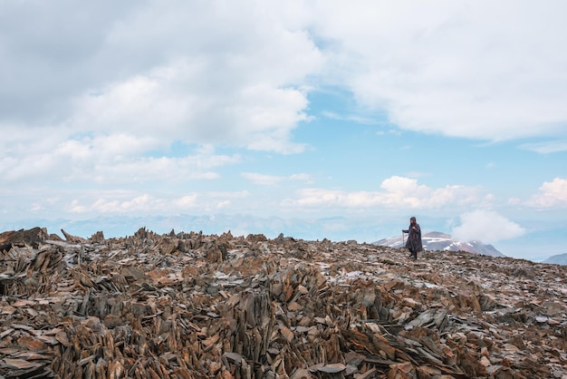 Szenische minimale Alpenlandschaft mit Touristen auf Steinhügel unter bewölktem Himmel Wanderer mit Trekkingstöcken in sehr großer Höhe Minimalistische Berglandschaft mit Mann auf Steinberggipfel unter Wolken