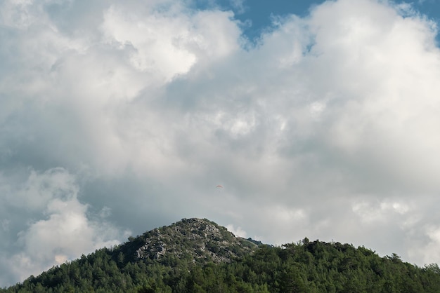 Szenischer Bergblick mit Gleitschirmen, die in großer Höhe fliegen, und weißen, flauschigen Wolken Panoramaaufnahme der Berge am Mittag an der Ägäisküste