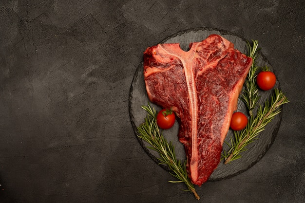 T-bone o Porterhouse con tomates y romero sobre un fondo negro.