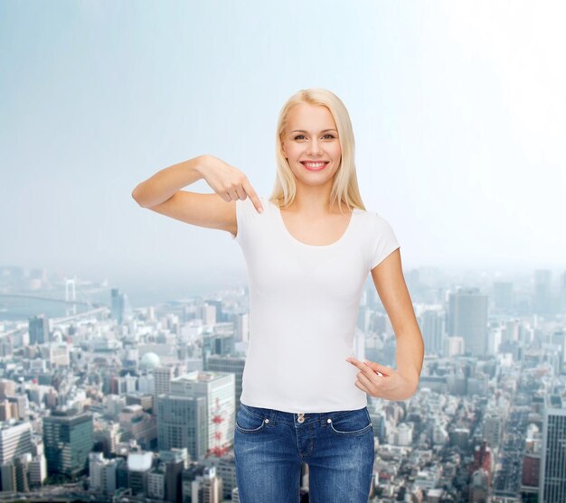 T-Shirt-Designkonzept - lächelnde junge Frau, die mit dem Finger auf ein leeres weißes T-Shirt zeigt