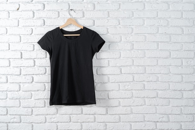 T-shirt preta pendurada em um cabide contra a parede de tijolos