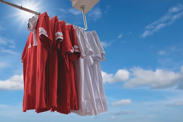 T-shirt vermelhos e brancos que penduram em uma corda com fundo do céu azul.