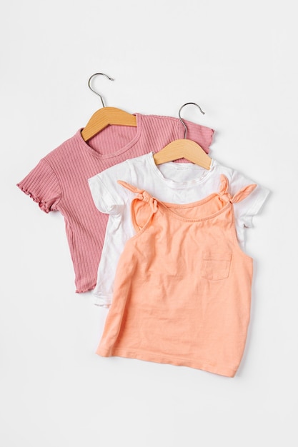 T-Shirts auf Kleiderbügel. Set Babykleidung und Accessoires für Frühling, Herbst oder Sommer auf weißem Hintergrund. Mode Kinder Outfit. Flache Lage, Ansicht von oben