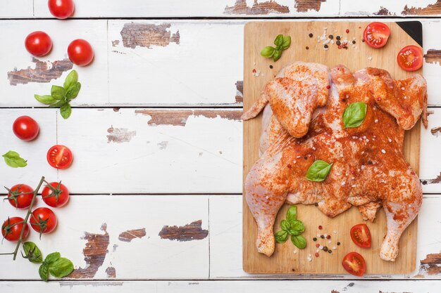 Tabaco de pollo crudo en una tabla de madera con especias y verduras Copiar espacio