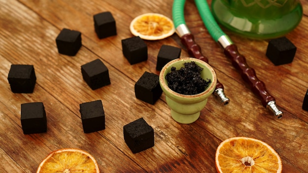 Tabaco en el recipiente para narguile sobre mesa de madera con carbón y rodajas de naranja secas