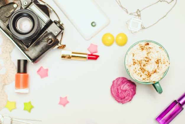 Tabela branca da mesa de escritório com smartphone, câmera do vintage, latte da especiaria e cosméticos.