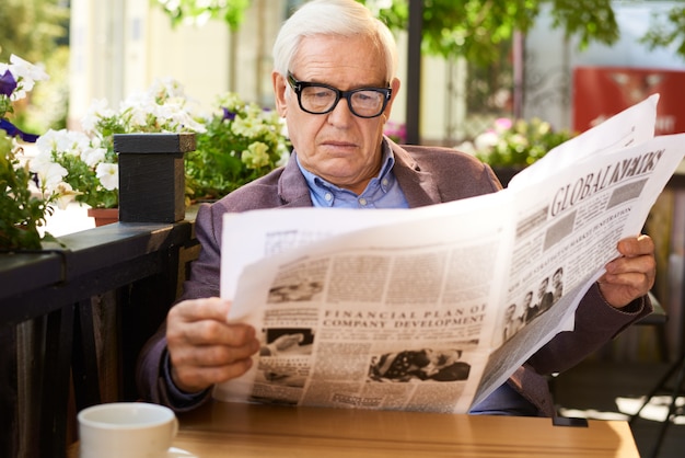 Tabela de aveia de jornal sênior homem lendo no café