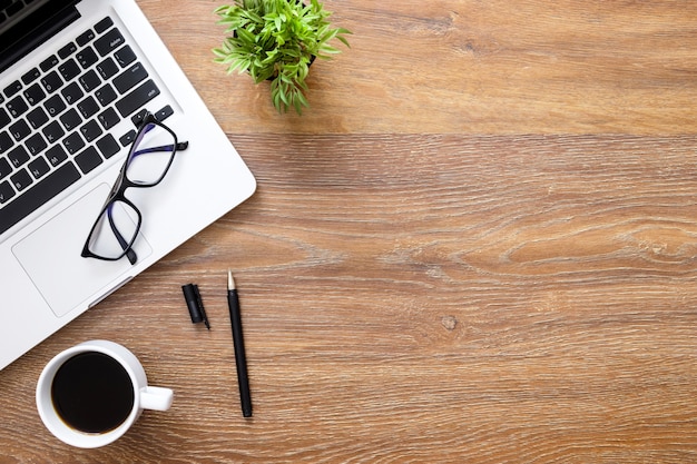 Tabela de mesa de escritório de madeira com laptop, xícara de café e suprimentos.