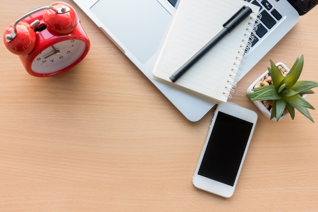 Foto tabela de mesa de escritório de madeira com telefone inteligente, caderno e caneta e alarme de relógio de tempo.