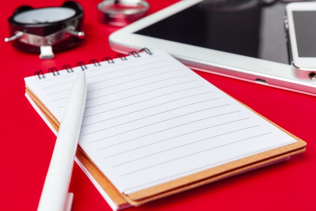 Tabela de mesa de escritório vermelho com caderno em branco, teclado e suprimentos.