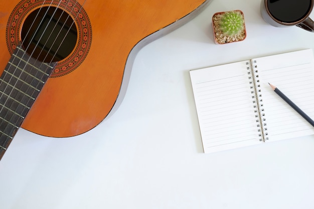 Tabela do escritor da música um espaço de trabalho com a guitarra acústica do músico e o copo de café com papel do bloco de notas na mesa da vista superior.