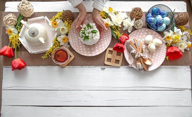 Tabelleneinstellung für die Osterferien. Tee, hausgemachter Kuchen, Eier und Blumen auf einem Holztisch kopieren Raum.