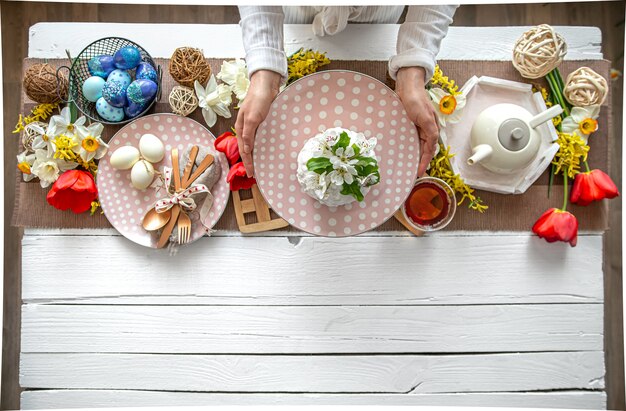 Tabelleneinstellung für die Osterferien. Tee, hausgemachter Kuchen, Eier und Blumen auf einem Holztisch.