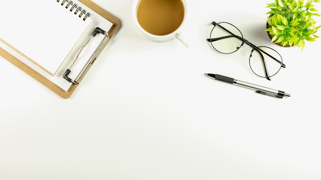 Tabla blanca del escritorio de oficina con una taza de café, una pluma, un cuaderno en blanco y vidrios.