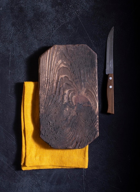 Tabla de cortar para cortar verduras y alimentos con un cuchillo rústico de fondo marrón oscuro con textura de madera natural