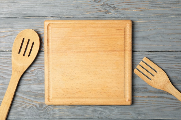 Tabla de cortar, cuchara y tenedor sobre fondo de madera