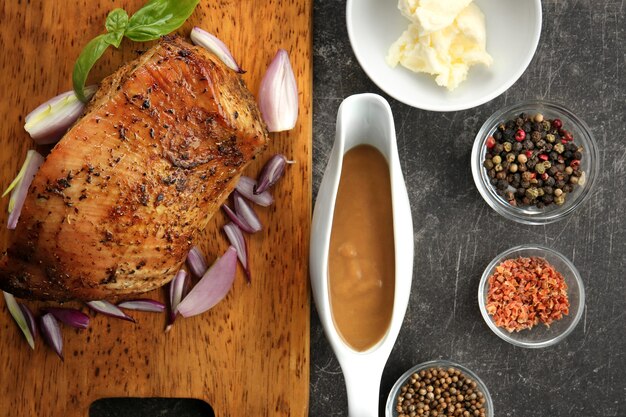 Tabla de cortar con delicioso pavo, especias y salsera en mesa gris