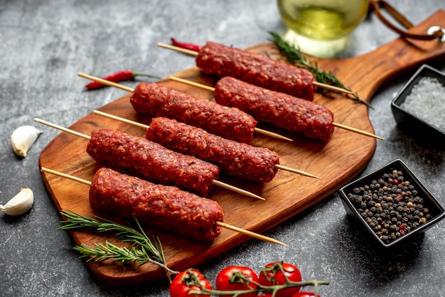 Una tabla de cortar de madera con carne y un tazón de pimienta negra al lado.