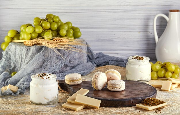 Tabla de cortar de madera cubierta con macarrones, yogur de chocolate y uvas