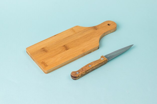 Tabla de cortar de madera y cuchillo con mango de madera sobre fondo azul.